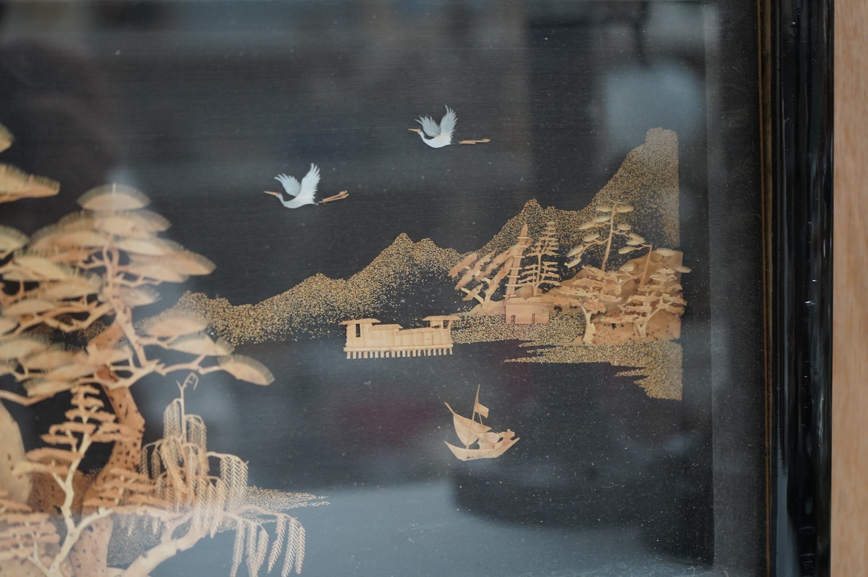 A Chinese framed, intricate relief cork landscape carving, of a Pagoda amongst trees by a river with junks and birds above., 41cm x 15cm